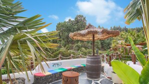 A patio with a stone floor, a wooden barrel, a thatched umbrella, and a colorful seating area.