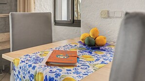 A dining table with a floral tablecloth, a notebook, and a bowl of fruit.