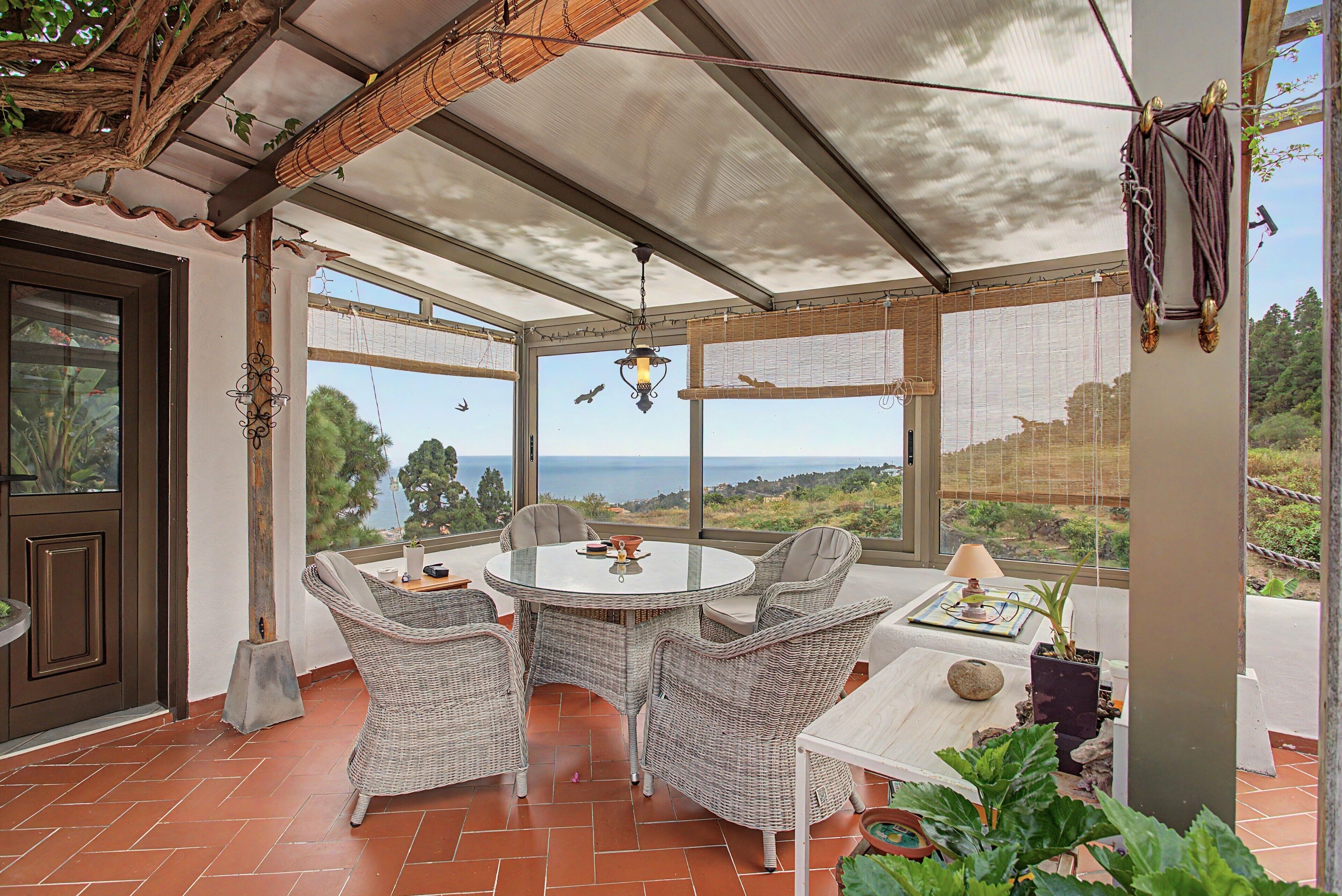 Un patio techado con muebles de mimbre, una mesa y vista al mar.