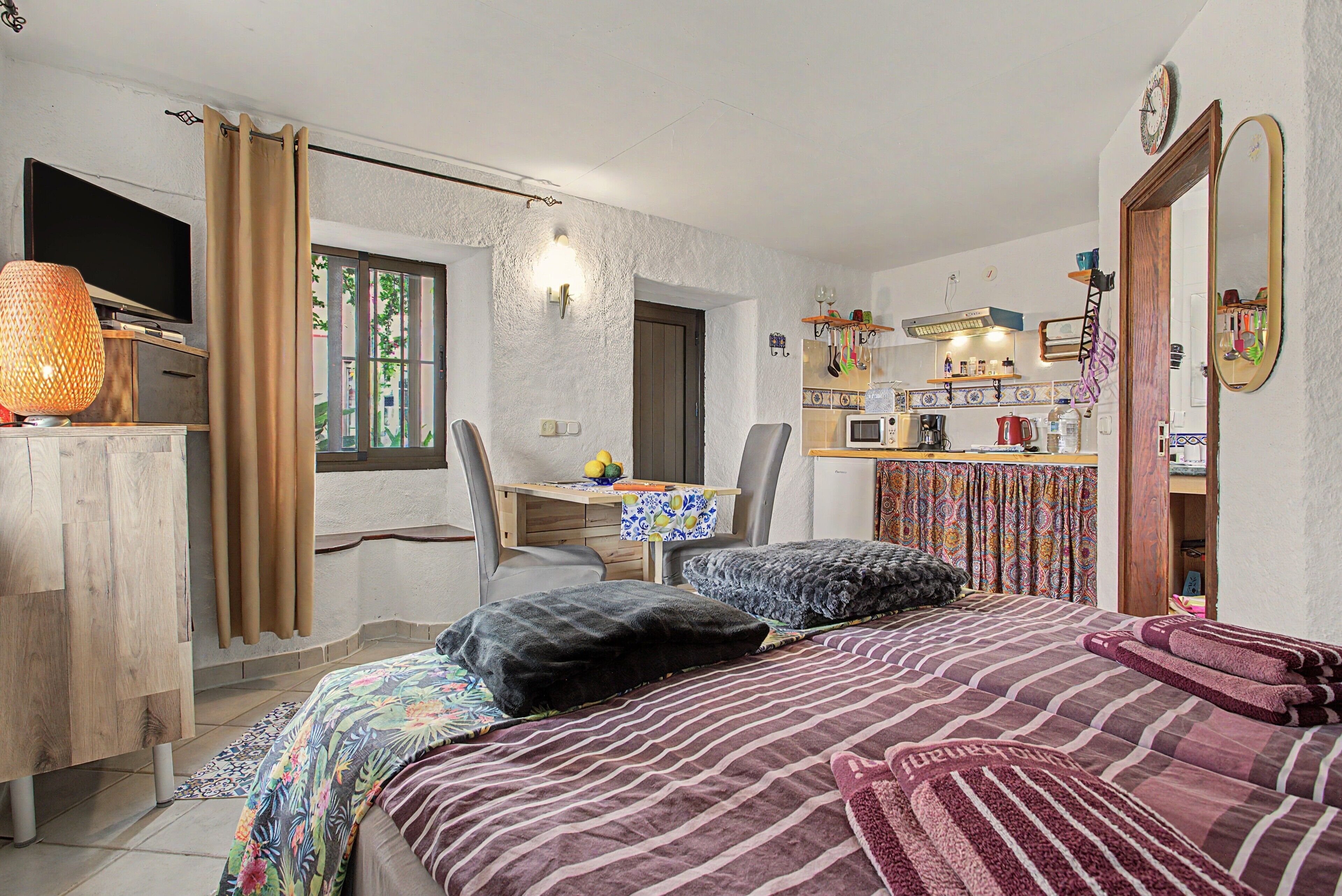 Un dormitorio con una cama, dos sillas, un escritorio y una kitchenette.