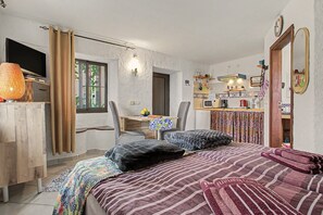 A bedroom with a bed, two chairs, a desk, and a kitchenette.