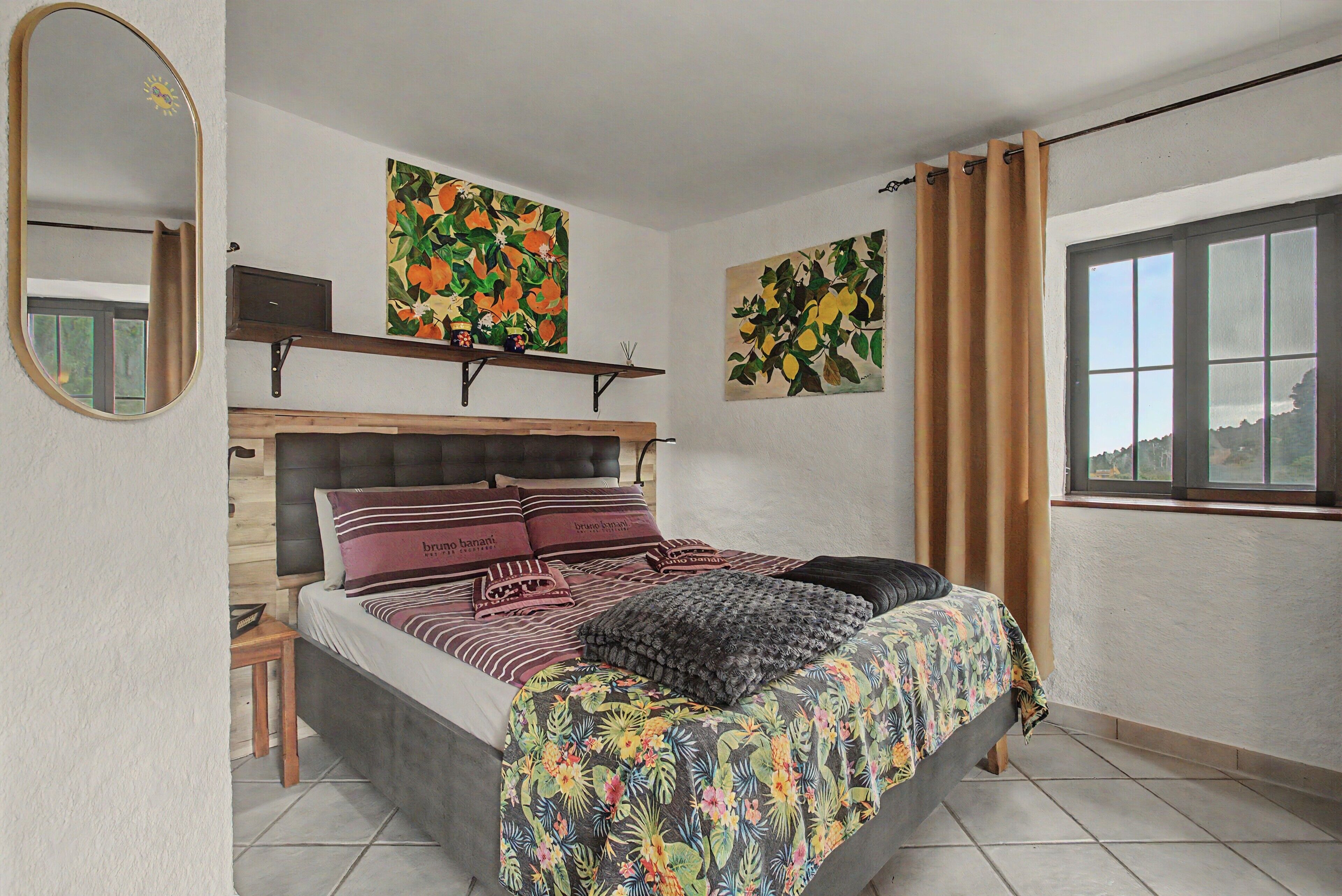 A bedroom with a bed, a nightstand, a mirror, and two paintings on the wall.