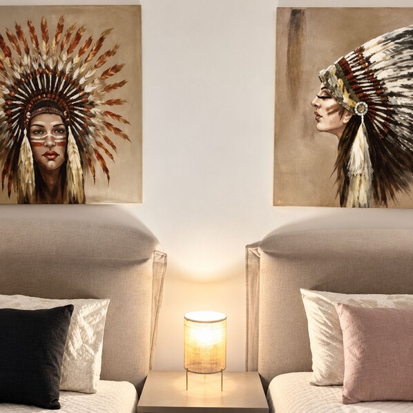 A hotel room with two beds, a nightstand with a lamp, and two paintings on the wall.