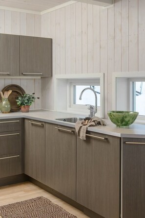A kitchen with wooden cabinets, a window above the sink, and a green bowl on the counter.