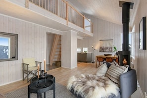 A spacious living area with a high ceiling, a fireplace, a dining table, and a staircase leading to an upper level.