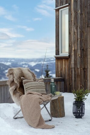 A cozy outdoor seating area with a chair covered in a blanket, a thermos, a mug, and a small potted plant.