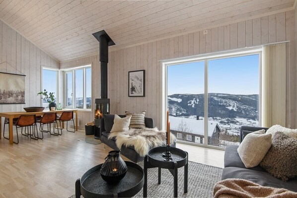 A spacious living room with a fireplace, large windows, and a view of a snowy landscape.
