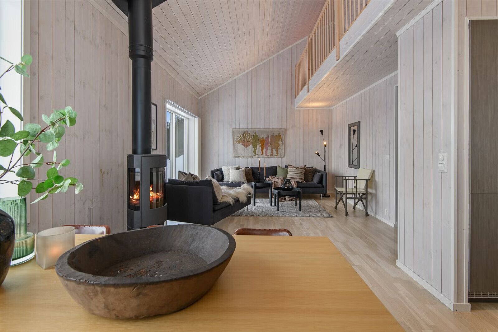 A modern interior with a wood-paneled room, a fireplace, a sofa, and a dining area.