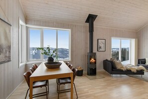 Ein gemütliches Wohnzimmer mit Kamin, Holzmöbeln und großen Fenstern mit Blick ins Freie.