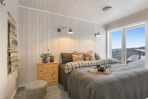 A bedroom with a large bed, a nightstand, a dresser, and a window with a view.
