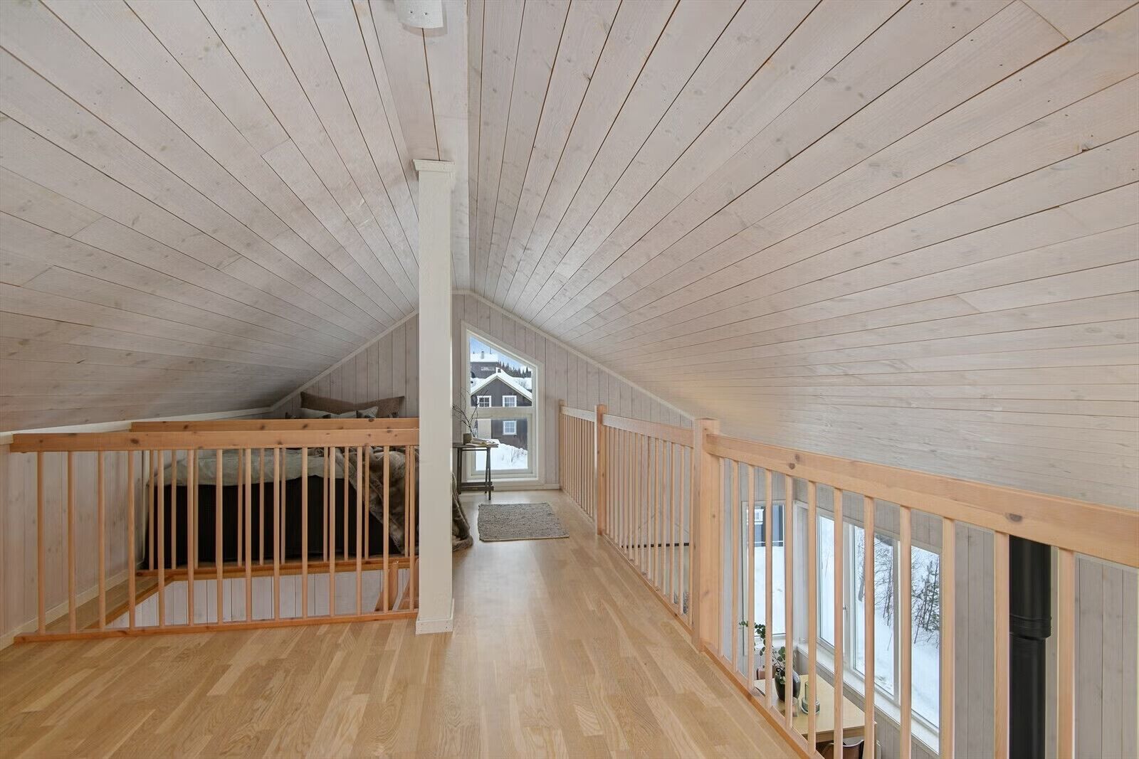 A high-ceilinged room with wooden floors and railings, a visible window, and a staircase leading to an upper level.