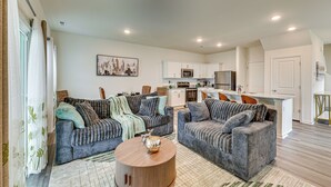 A modern living room with two grey sofas, a coffee table, and a kitchen in the background. - 2 Townhome Retreat | Sleeps 12 | 40 Min to Raleigh (Wilson)