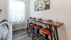 A dining area with a wooden table, four stools, and a painting of flowers on the wall. - 2 Townhome Retreat | Sleeps 12 | 40 Min to Raleigh (Wilson)