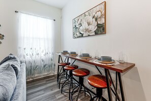 Ein Essbereich mit einem Holztisch, vier Hocker und einem Blumenbild an der Wand.