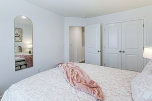 Ein Schlafzimmer mit einem Bett, einem Spiegel, einem Kleiderschrank und einer Tür zu einem weiteren Raum.