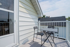 En balkon med et bord og to stole, et hvidt gelænder og udsigt til himlen.
