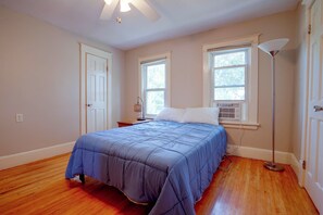 A bedroom with a bed, a nightstand, a lamp, and a window with blinds. - Twin Cities Duplex Near Downtown Minneapolis (Saint Paul)