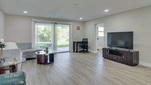 Una sala de estar moderna con un sofá, una mesa de centro, televisor y un ventanal corredero que da a un patio.