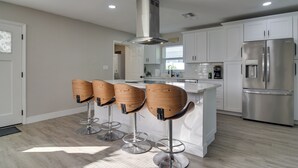 Una cocina moderna con alacenas blancas, un refrigerador de acero inoxidable y cuatro taburetes de madera.