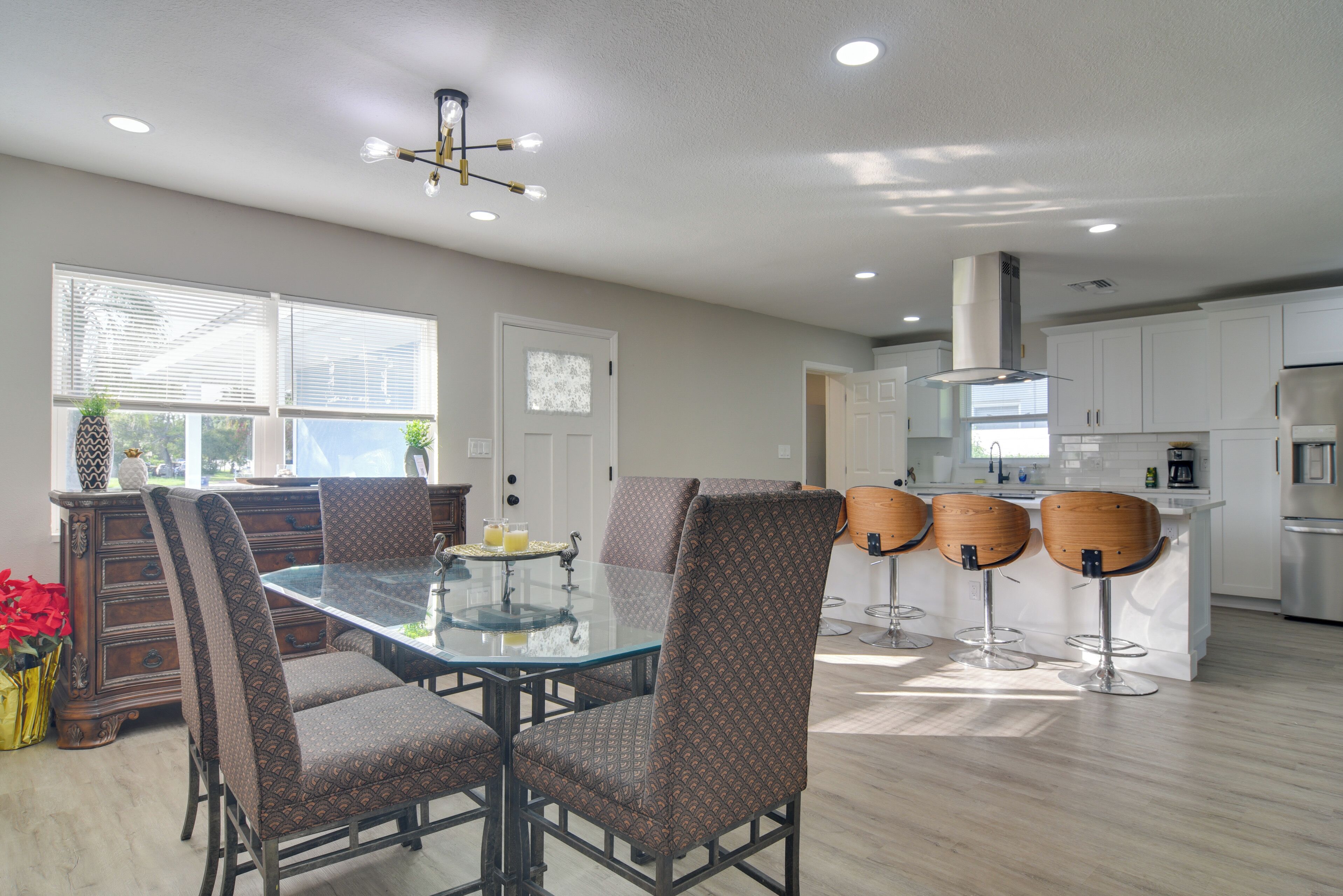 A modern kitchen with white cabinets, a glass-top dining table, and four bar stools.