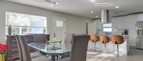 A modern kitchen with white cabinets, a glass-top dining table, and four bar stools.