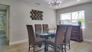 Un comedor con una mesa de vidrio y sillas estampadas, un adorno en la pared y una ventana con persianas.