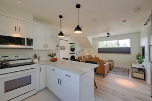 A modern kitchen with white cabinetry, a built-in oven, and a large island with a bowl of fruit. - 1 Mi to UM Campus! Newly Built Apt w/ Side Yard (Missoula)