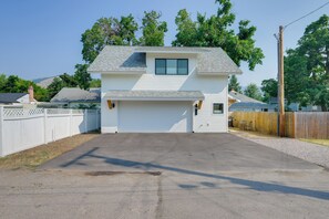 Une maison à deux étages avec un garage, entourée d’une clôture en bois et donnant sur une allée gravillonnée.