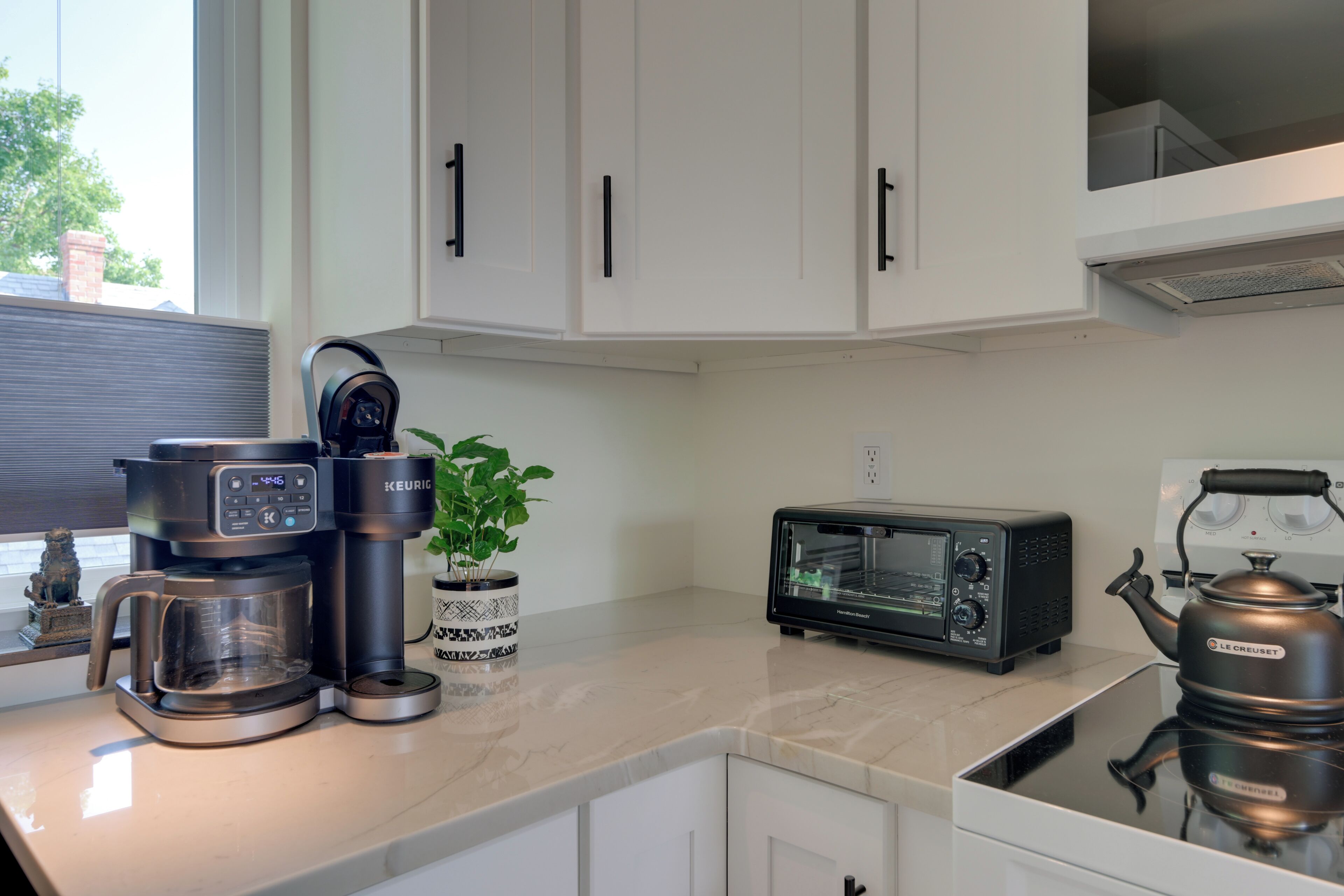 Una cocina con cafetera, tostadora, hervidor y una planta en maceta sobre la encimera.