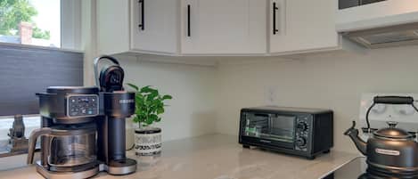Una cocina con cafetera, tostadora, hervidor y una planta en maceta sobre la encimera.