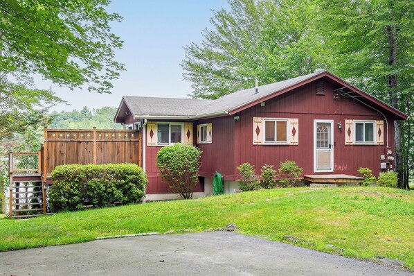 A single-story house with a red exterior, a front porch, and a fenced yard. - Lakefront Family Home w/ Docks in Barnstead! (Barnstead)