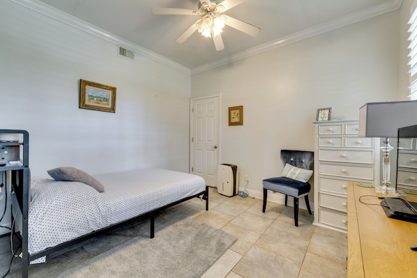 A bedroom with a bed, a desk, a chair, a dresser, and a ceiling fan.