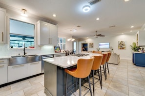 A modern kitchen with a large island, bar stools, and a dining area with a sofa and chairs.