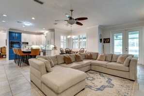 Uma cozinha moderna com armários brancos, uma sala de jantar com mesa e cadeiras, e uma sala de estar com sofá seccional bege.