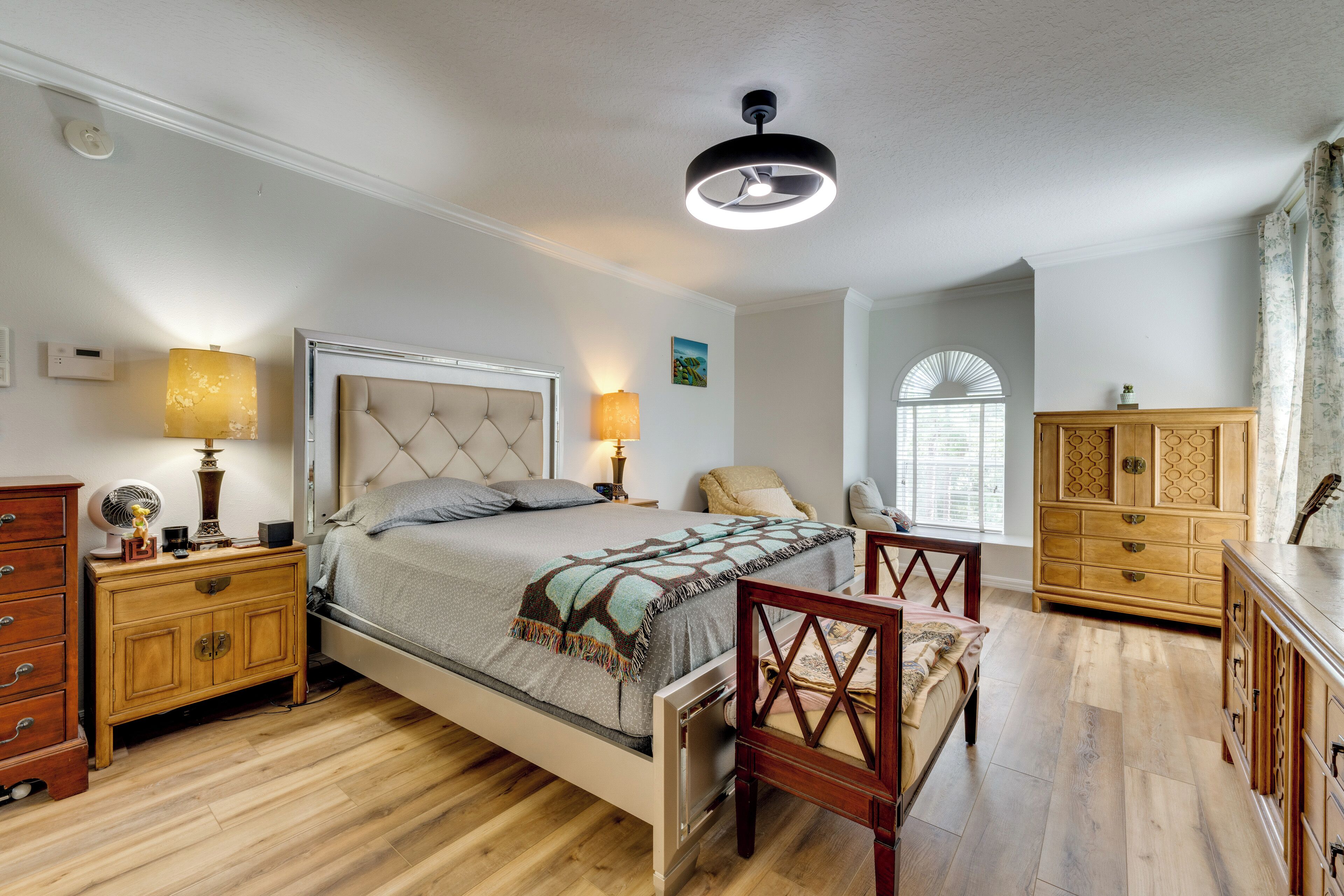 Een slaapkamer met een bed, nachtkastjes, een stoel, een kledingkast en een plafondventilator.