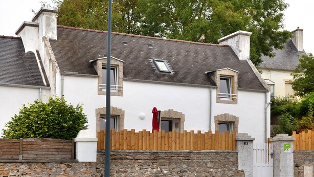 Una casa de dos pisos con base de pared de piedra, cerca de madera y puerta roja.