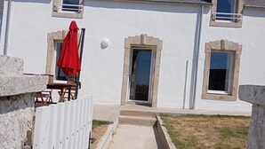 Um edifício branco com fachada de pedra, um guarda-chuva vermelho e uma porta que dá para uma entrada coberta.