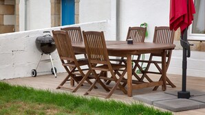 Una mesa de madera al aire libre con sillas, una parrilla y una sombrilla roja.