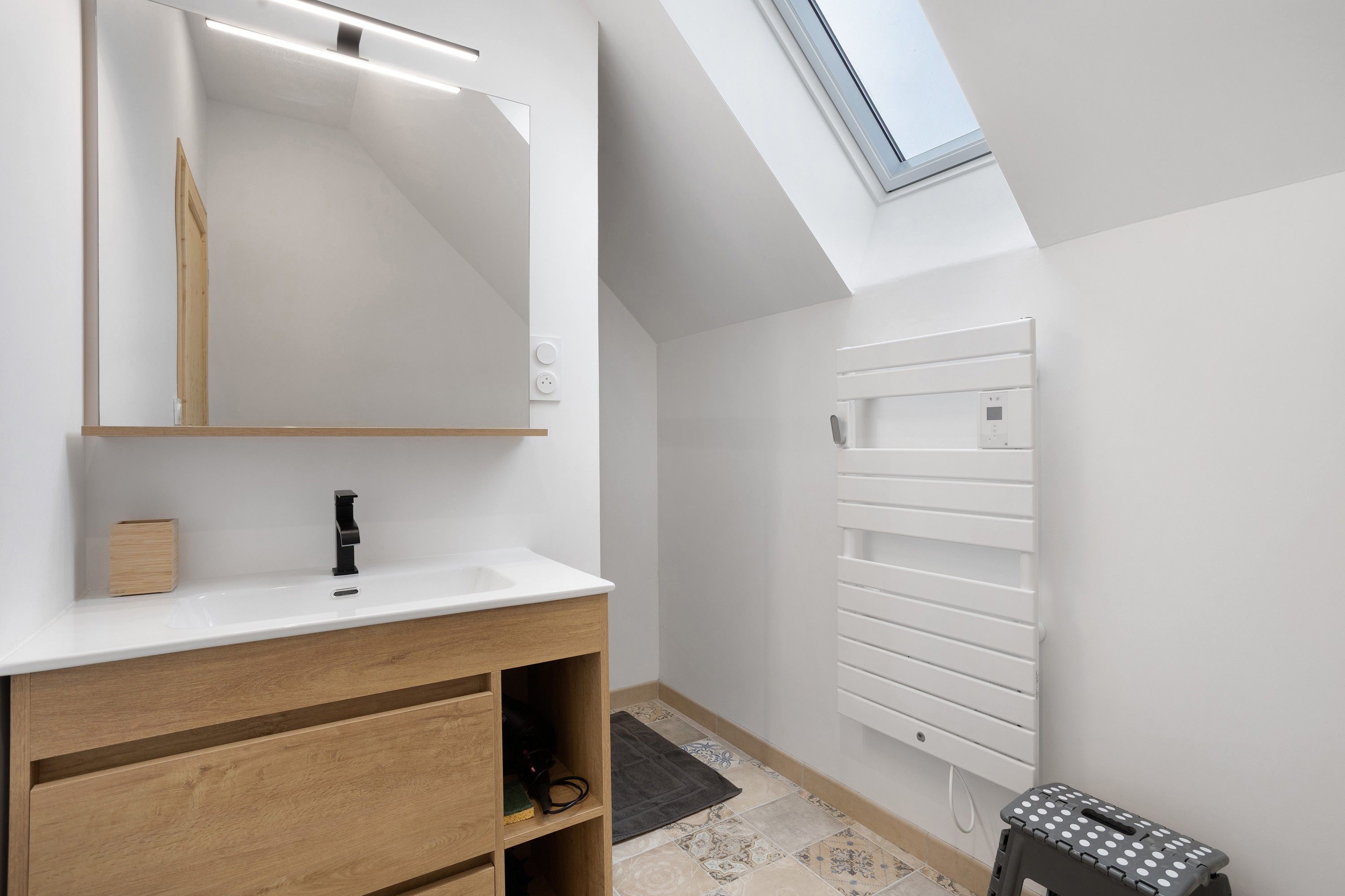 Een moderne badkamer met dakraam, grote spiegel, houten wastafelmeubel en handdoekhouder.