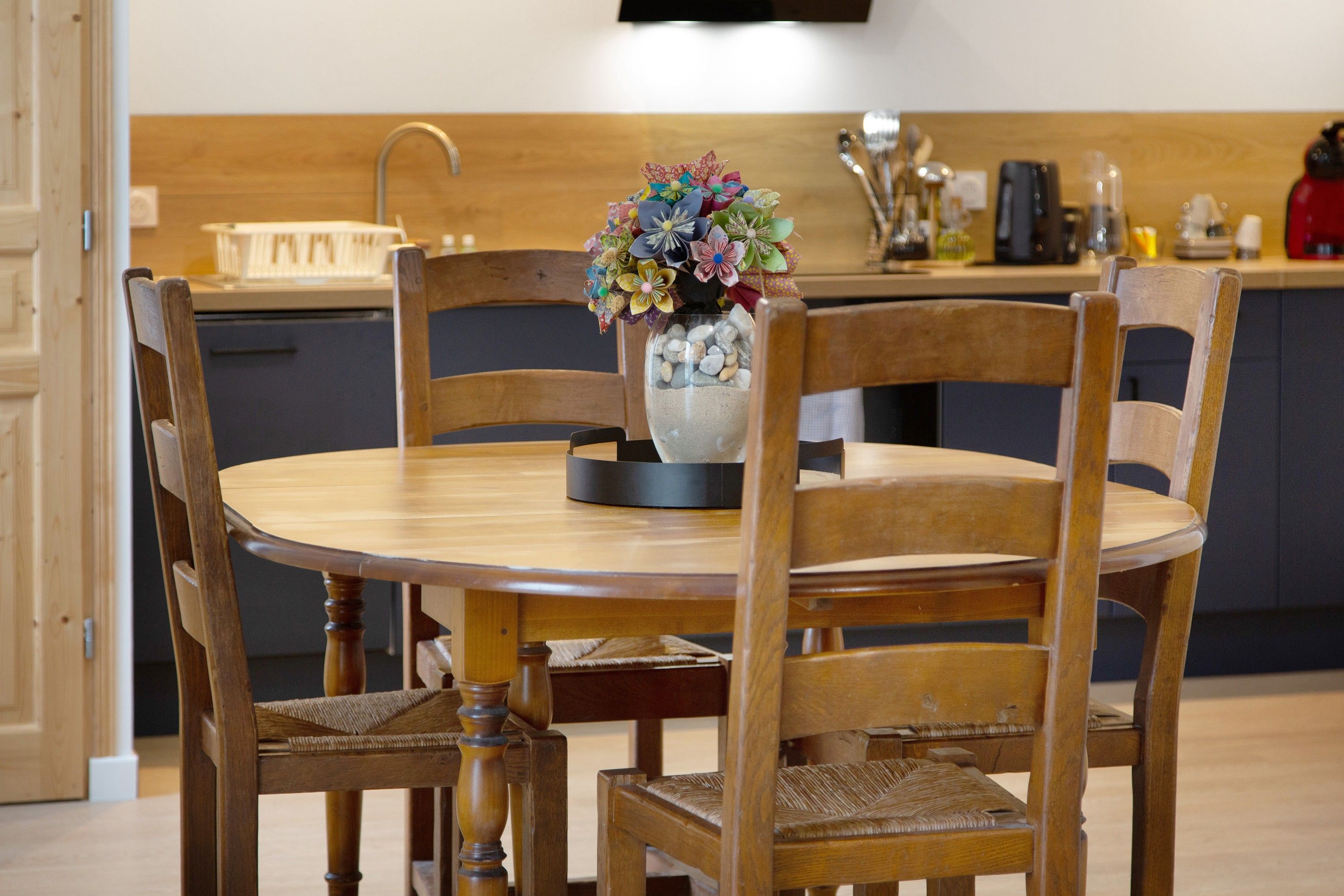 Ein runder Holztisch mit einer Blumenvase in der Mitte, umgeben von Holzstühlen.