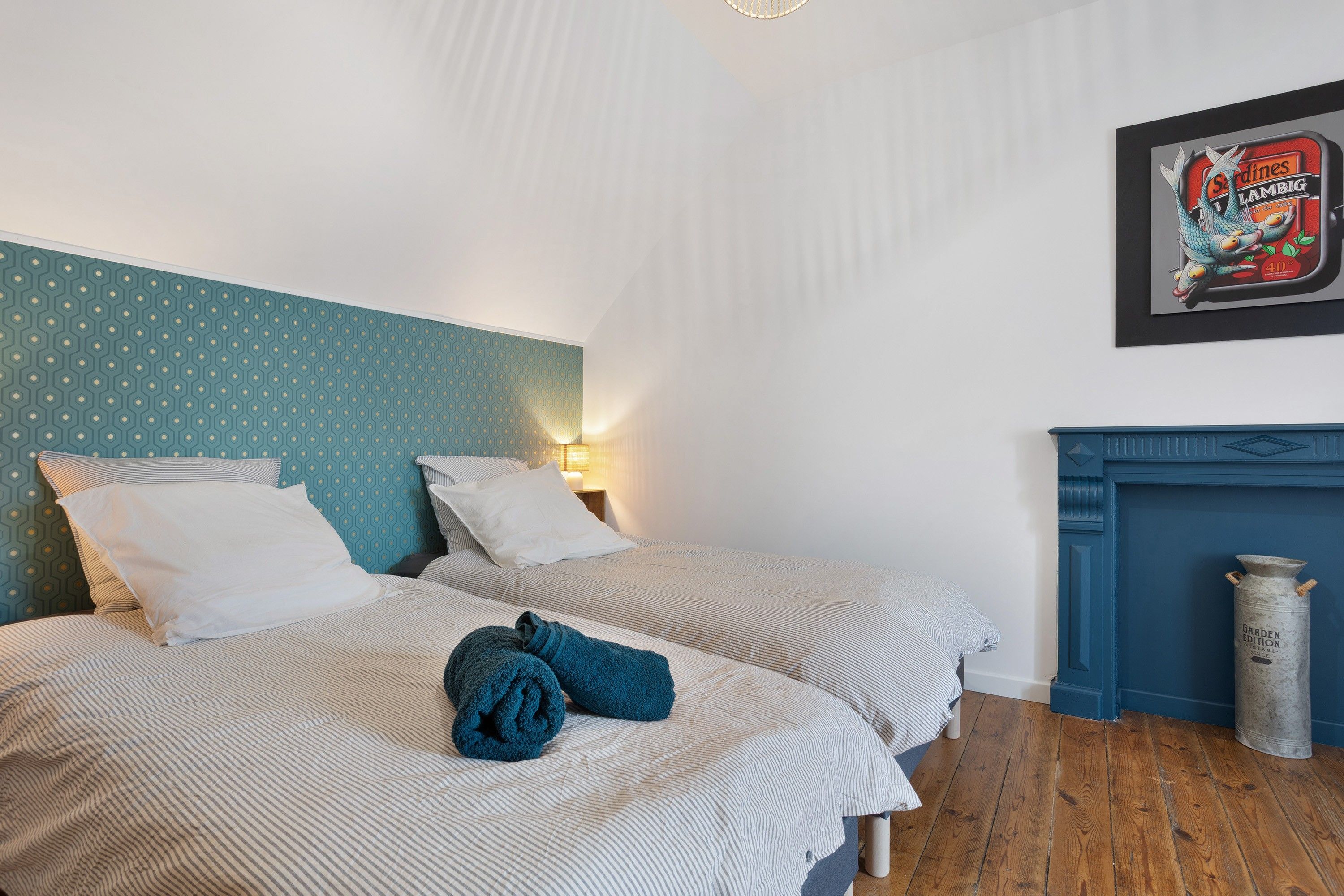 A bedroom with two beds, a patterned headboard, a framed picture on the wall, and a blue fireplace.