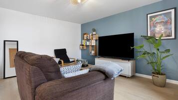 Un salon moderne avec un canapé marron, un fauteuil noir, un téléviseur à écran plat, une bibliothèque et une plante en pot.