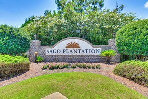 Placa para Sago Plantation, com muro de tijolos e vegetação.