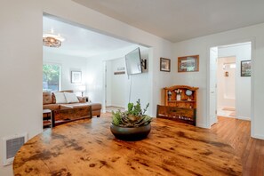 Uma sala de estar ampla com piso de madeira, um sofá de couro, uma mesa de centro com uma planta e uma TV fixada na parede.