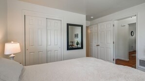 A bedroom with a bed, a nightstand, a lamp, a mirror, and a door leading to another room. - Walk to Dtwn Corvallis: Home Near OSU & Riverwalk (Corvallis)