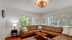 A living room with a brown leather sectional sofa, a wooden coffee table, a patterned rug, and a wall-mounted clock. - Walk to Dtwn Corvallis: Home Near OSU & Riverwalk (Corvallis)