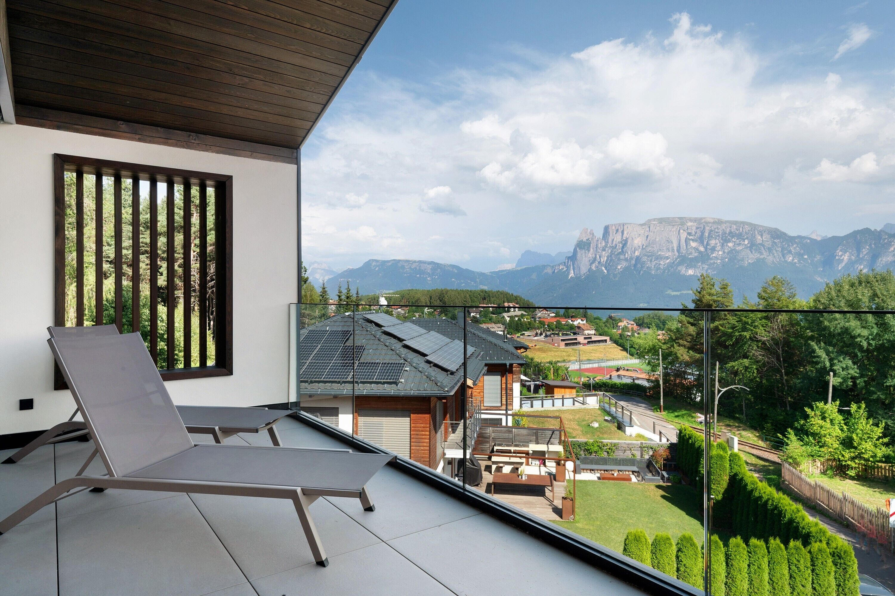 A balcony with a view of a mountain range, a lounge chair, and a wooden ceiling.