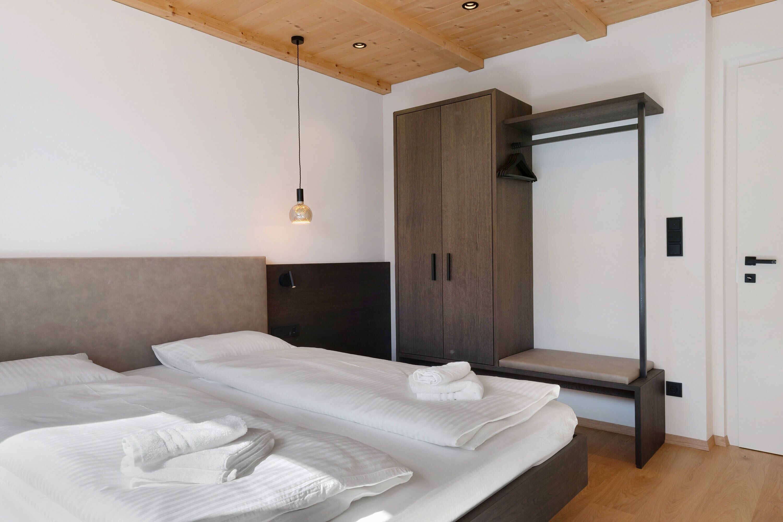 A modern bedroom with a large bed, a wardrobe, and a hanging light fixture.