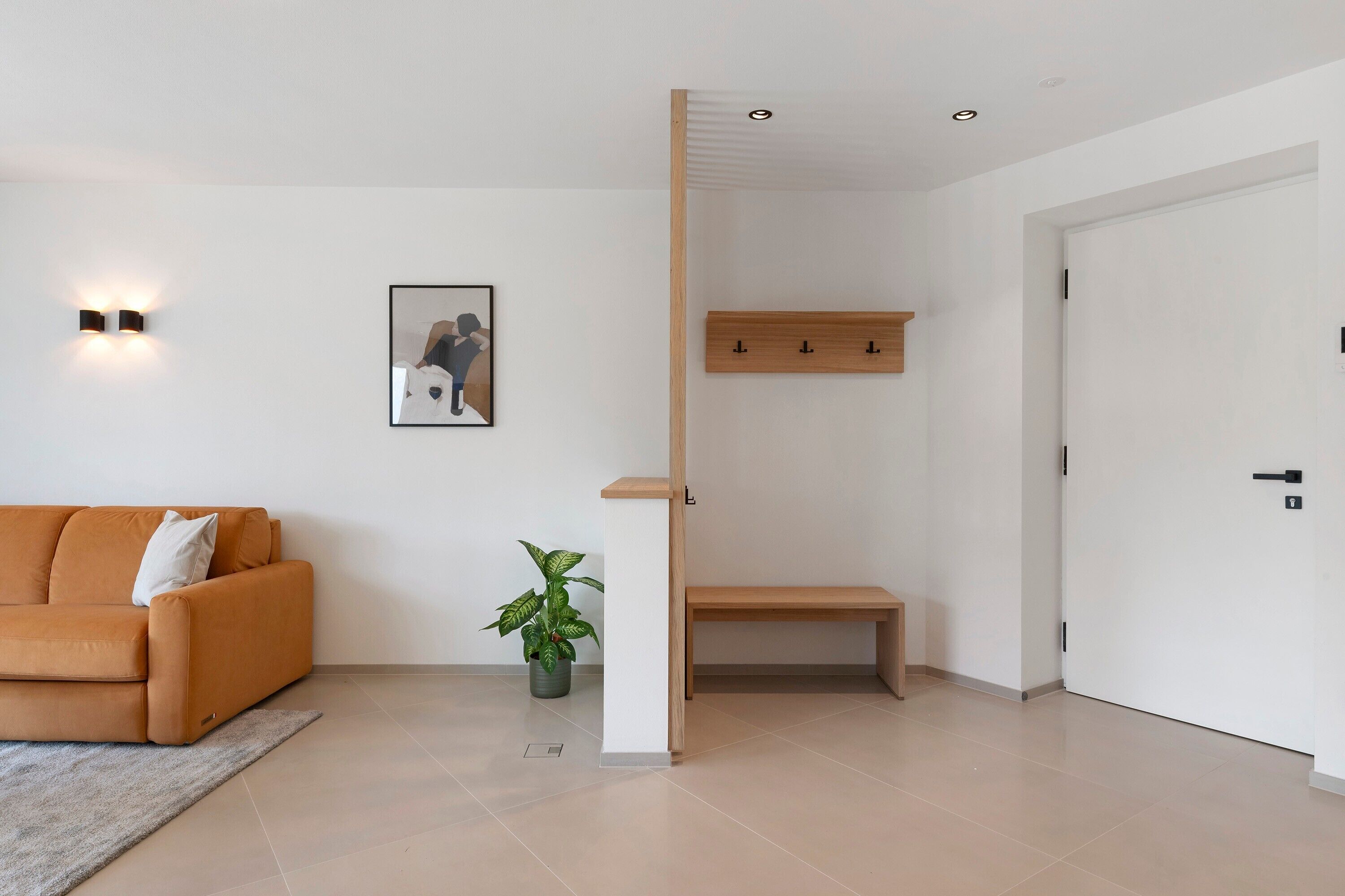 A modern living room with a sofa, a small table, a potted plant, and a wall-mounted picture.