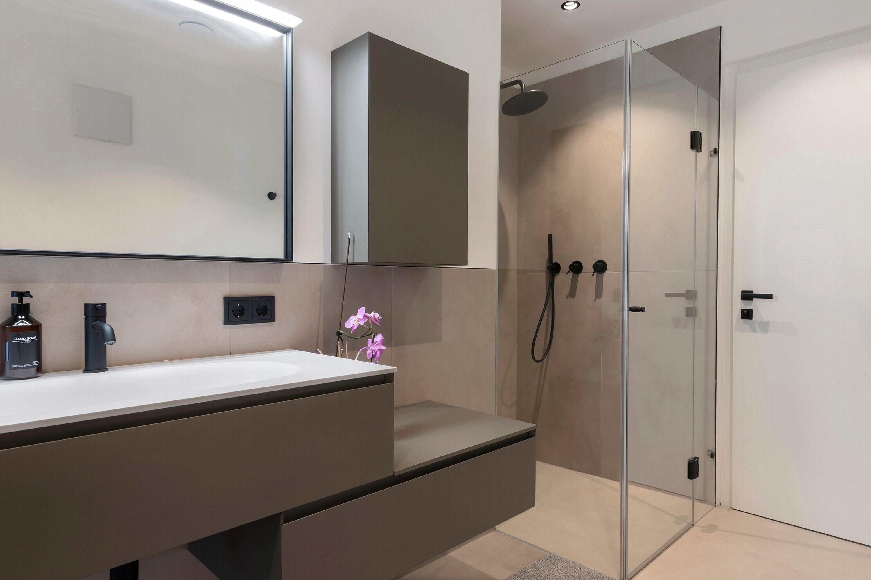 A modern bathroom with a glass shower enclosure, a white vanity with a dark countertop, and a large mirror above the vanity.
